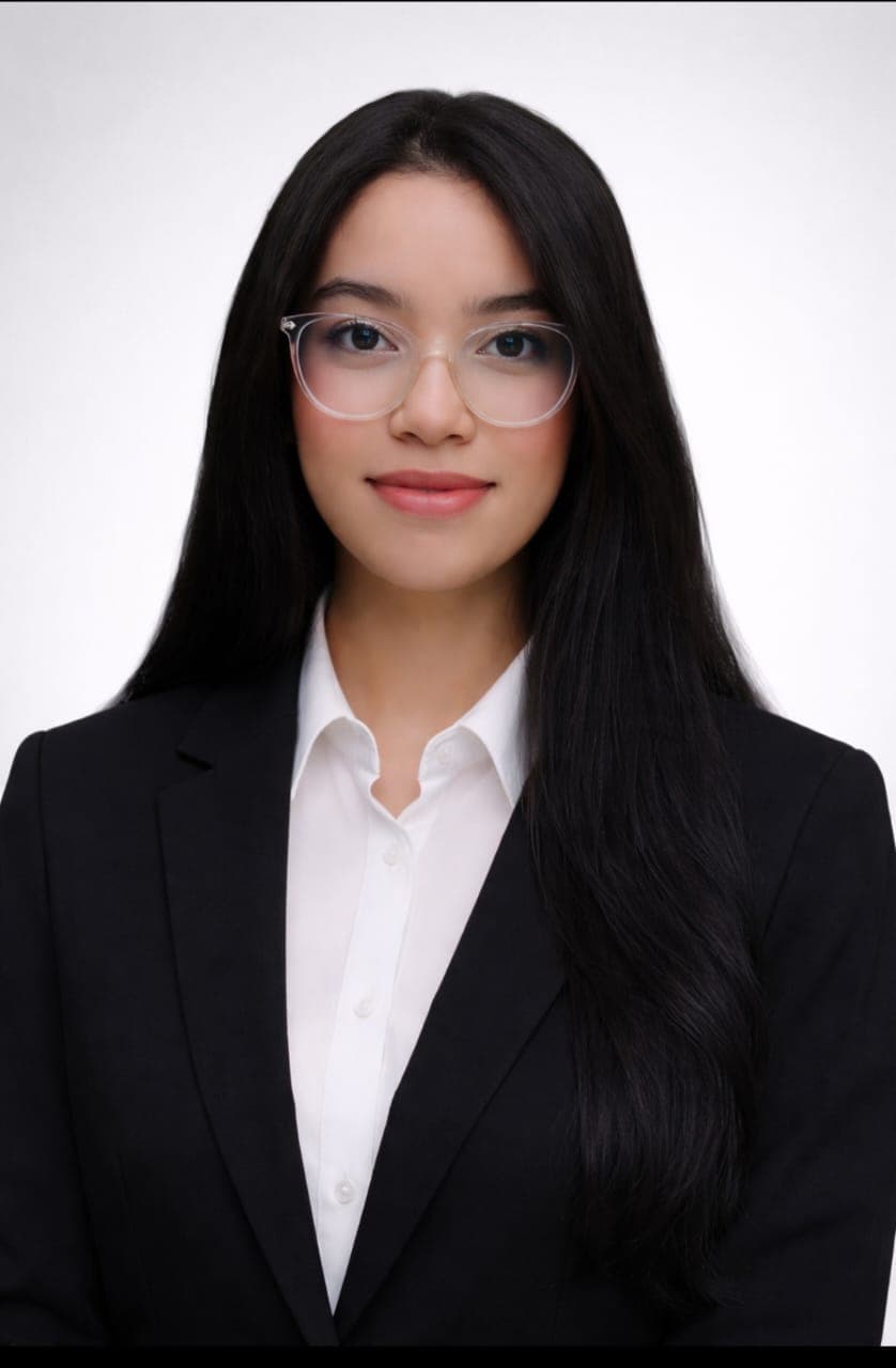 Junge Frau mit Brille, langen schwarzen Haaren, weißer Bluse und schwarzem Blazer vor weißem Hintergrund.