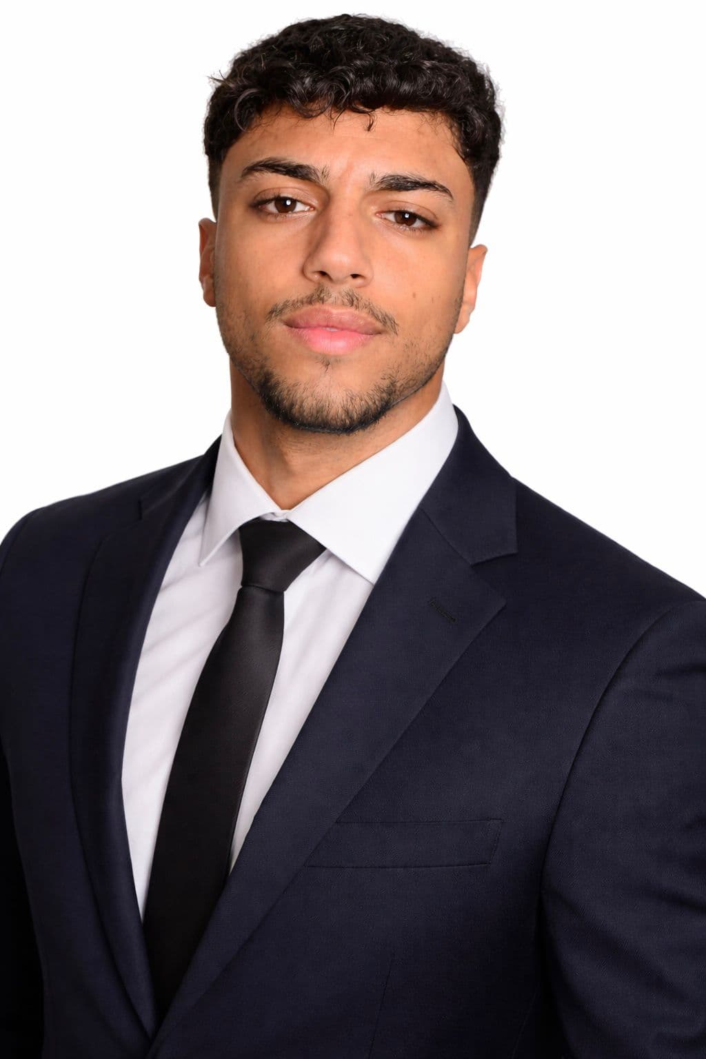 Junger Mann mit dunklen lockigen Haaren in einem dunkelblauen Anzug, weißem Hemd und schwarzer Krawatte.